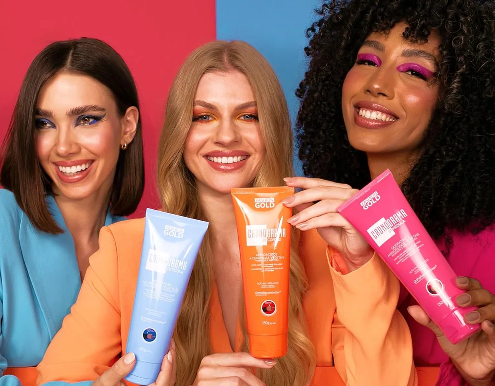 Three smiling models holding the blue, orange and pink Cronograma mask tubes