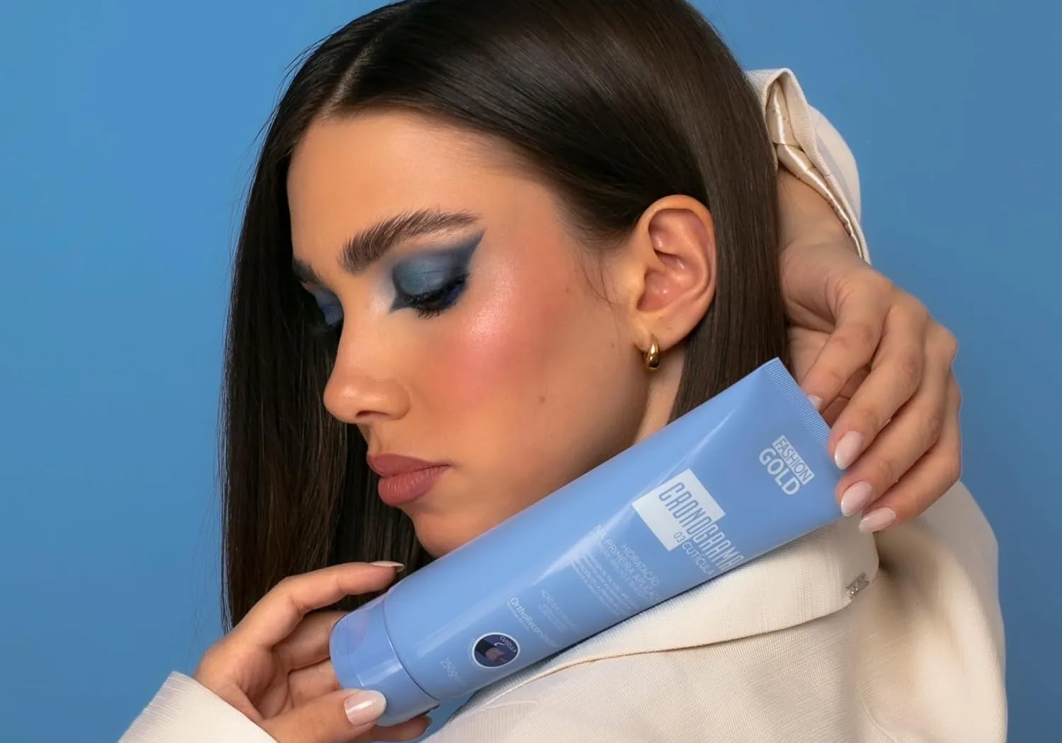 A dark-haired model holding the blue Cronograma Cuticula tube against her shoulder
